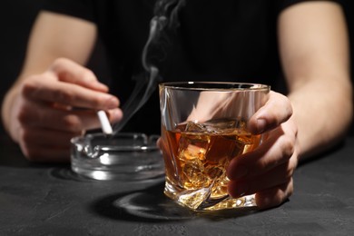 Photo of Alcohol addiction. Man with glass of whiskey and smoldering cigarette at dark textured table, selective focus