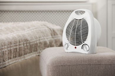 Photo of Modern electric fan heater on pouf in cozy room. Space for text