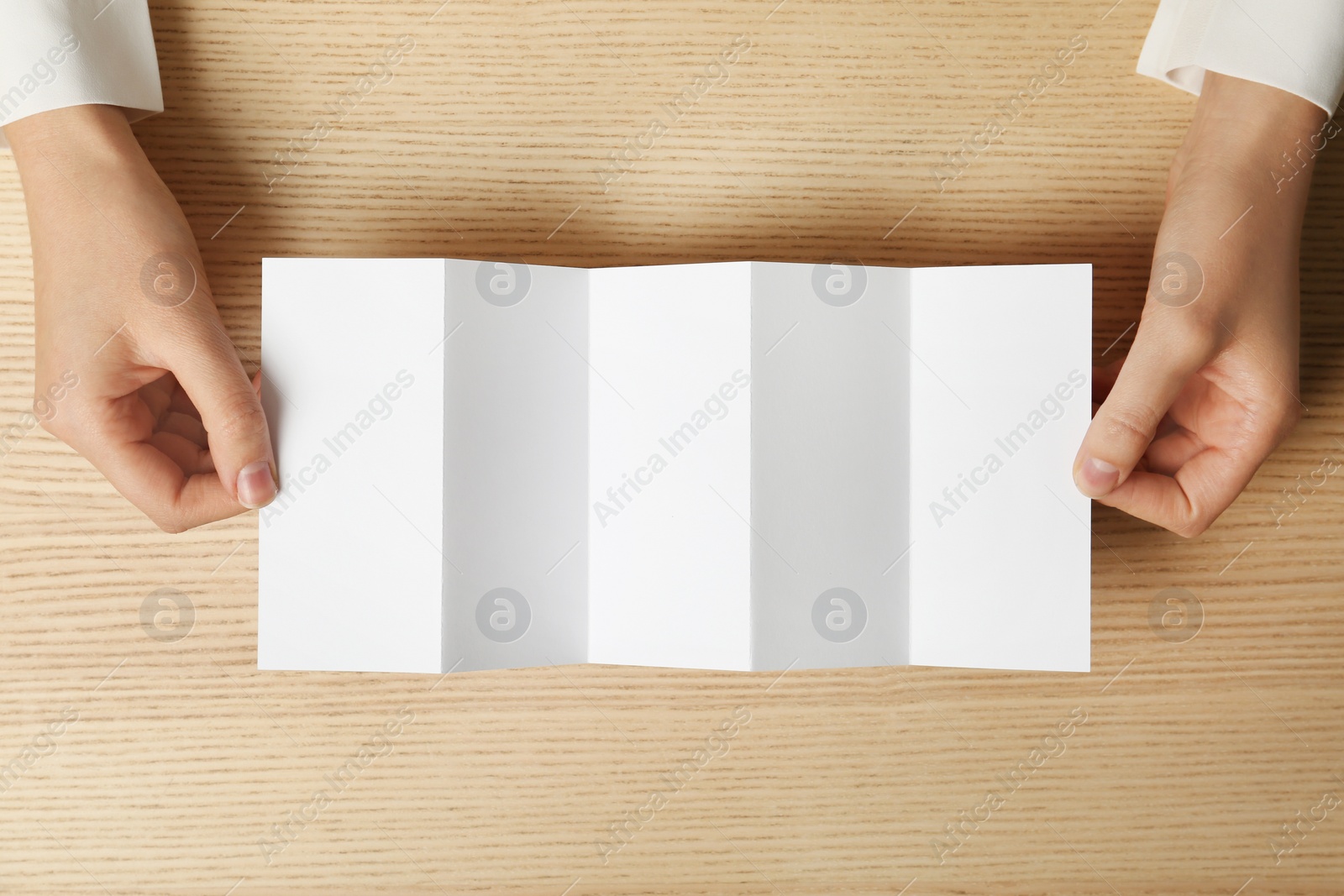 Photo of Woman holding blank brochure mock up on wooden table, top view