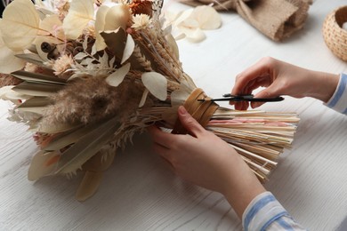 Photo of Florist making beautiful bouquet of dried flowers at white table, closeup