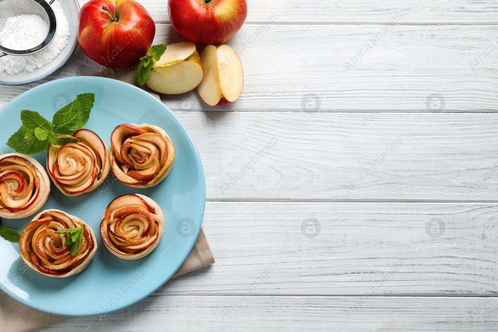 Photo of Freshly baked apple roses on white wooden table, flat lay. Space for text