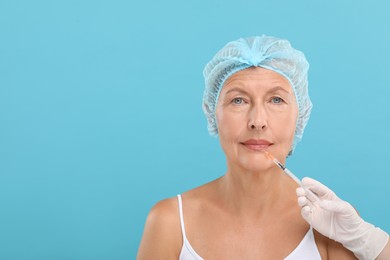 Photo of Doctor giving lips injection to senior woman on light blue background, space for text. Cosmetic surgery