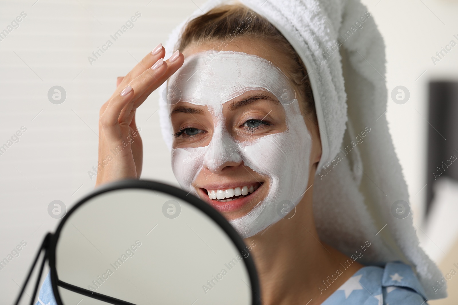 Photo of Young woman with face mask looking into mirror indoors. Spa treatments