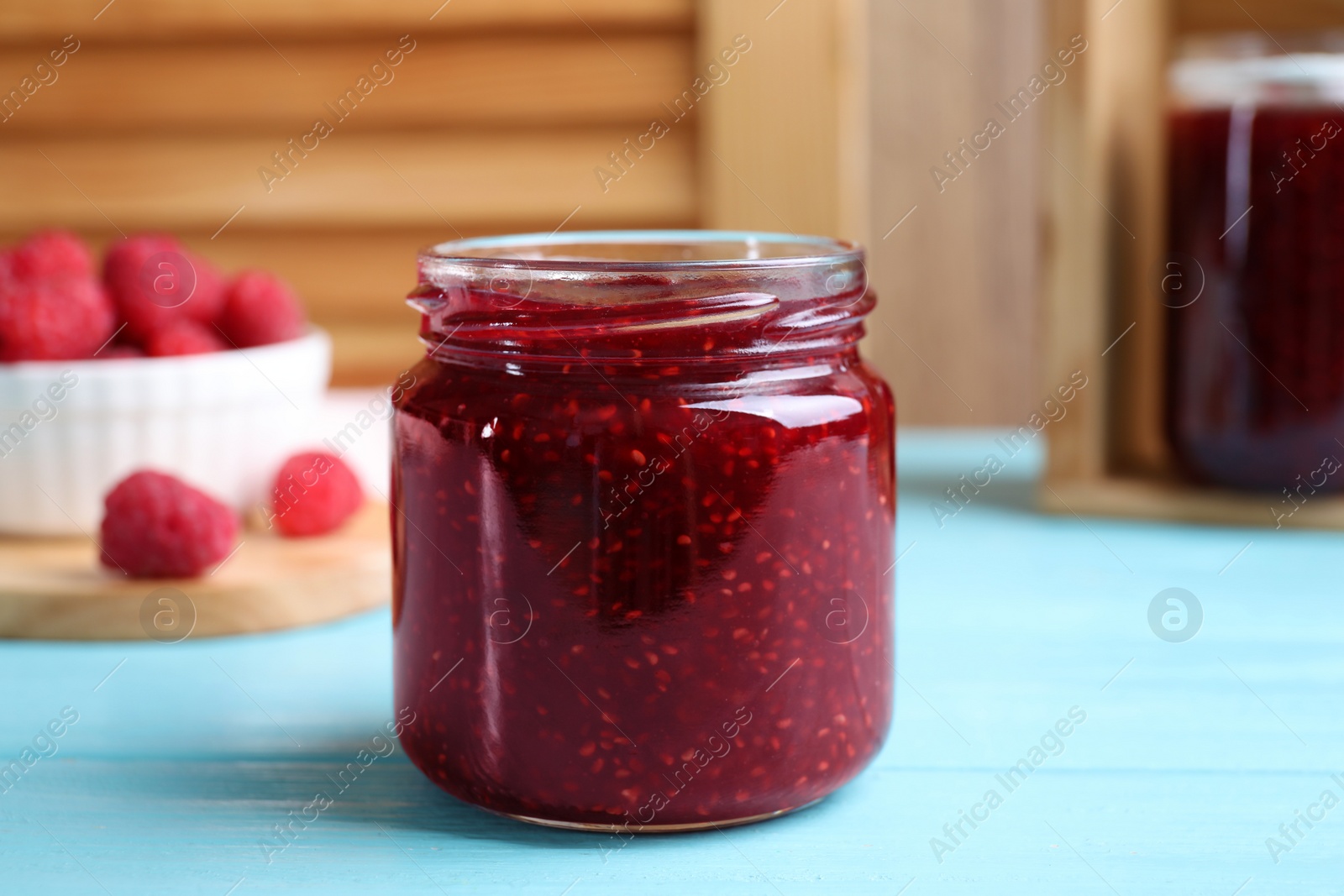 Photo of Delicious raspberry jam on light blue wooden table, closeup