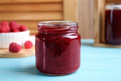 Photo of Delicious raspberry jam on light blue wooden table, closeup