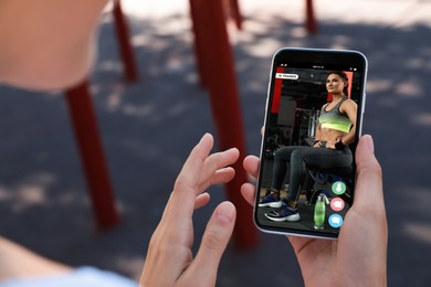 Image of Woman having workout with personal trainer via smartphone outdoors, closeup