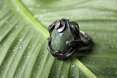 Photo of Beautiful silver ring with opal gemstone on green leaf, closeup