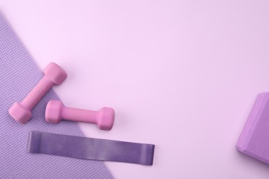 Two dumbbells, yoga block, mat and fitness elastic band on violet background, flat lay. Space for text