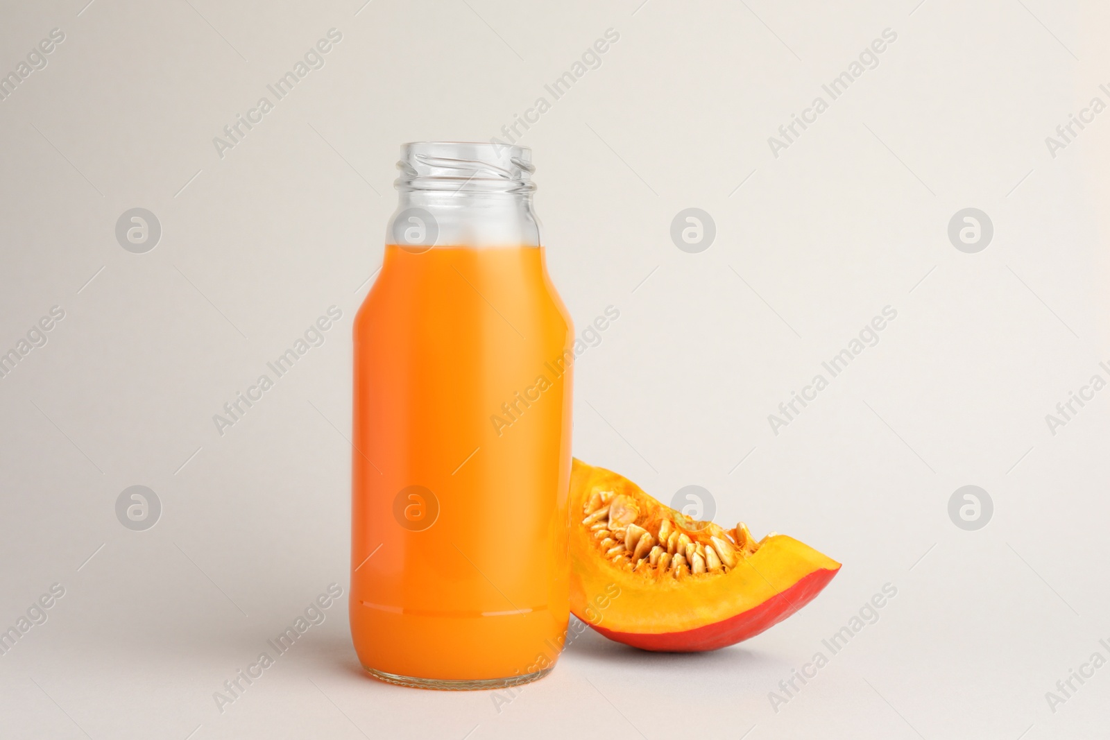 Photo of Tasty pumpkin juice in glass bottle and cut pumpkin on light background