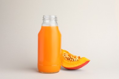 Photo of Tasty pumpkin juice in glass bottle and cut pumpkin on light background