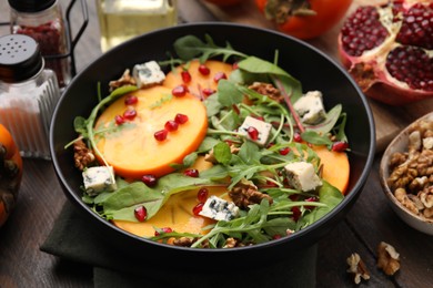 Tasty salad with persimmon, blue cheese, pomegranate and walnuts served on wooden table