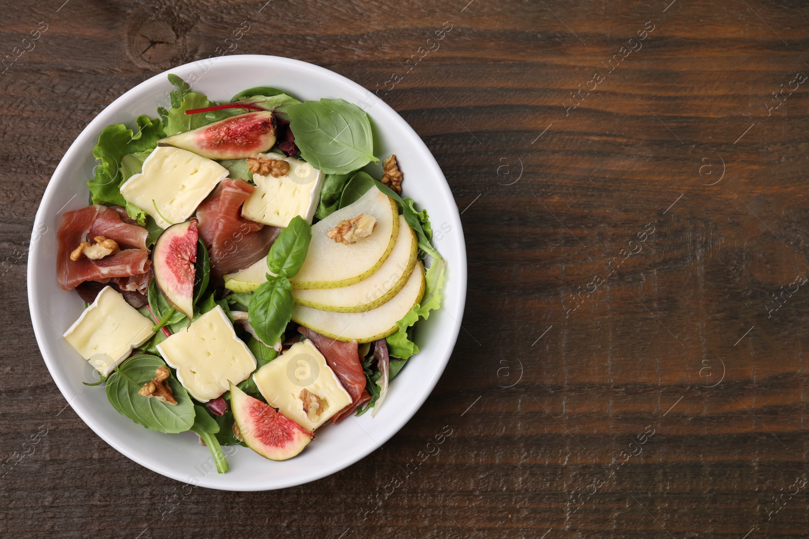 Photo of Tasty salad with brie cheese, prosciutto, pear and figs on wooden table, top view. Space for text
