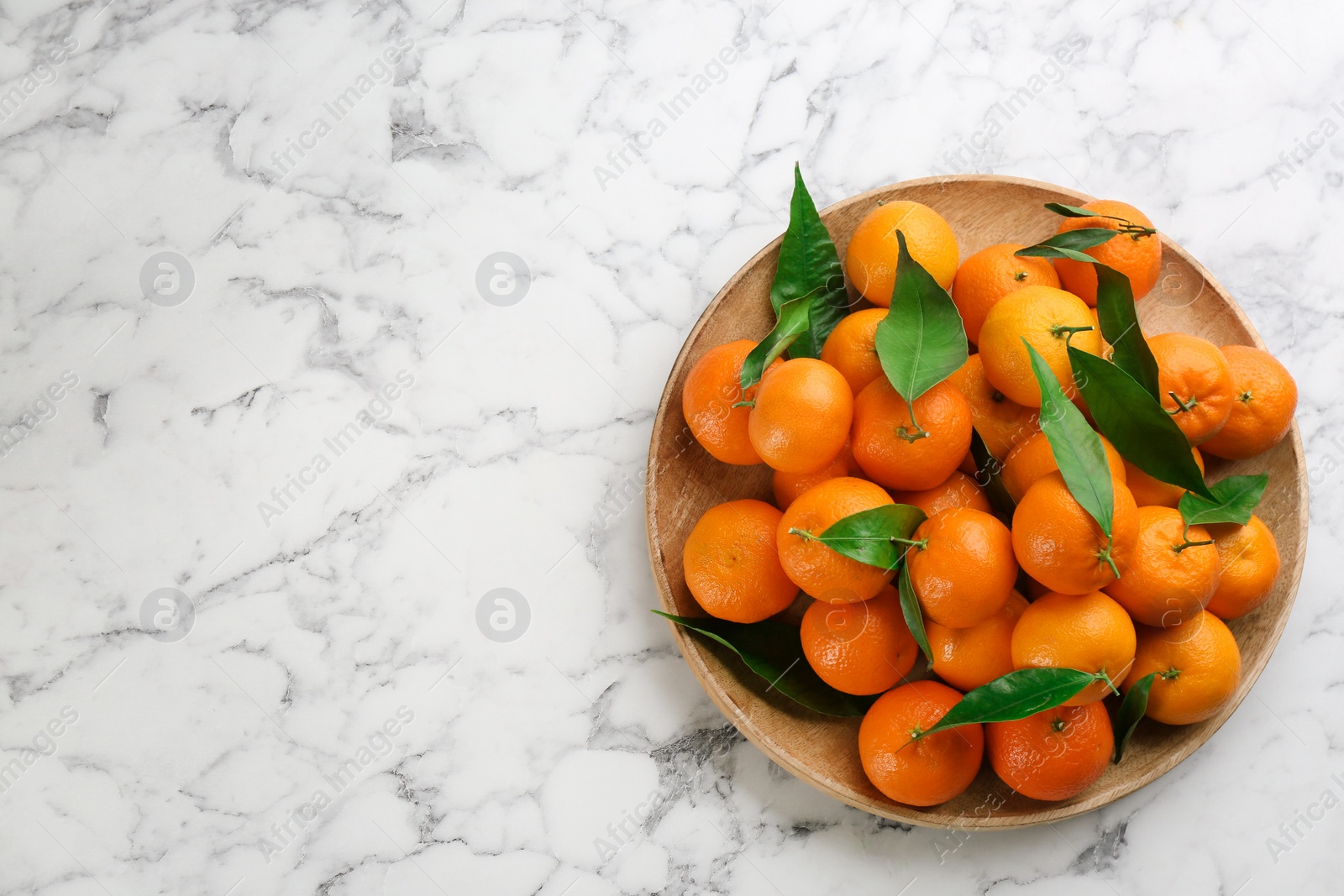 Photo of Fresh ripe tangerines with green leaves on white marble table, top view. Space for text