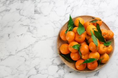 Photo of Fresh ripe tangerines with green leaves on white marble table, top view. Space for text