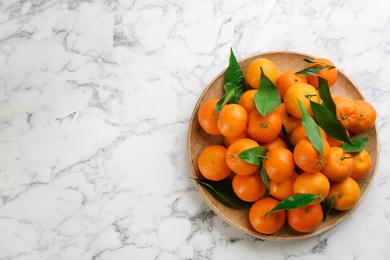 Fresh ripe tangerines with green leaves on white marble table, top view. Space for text