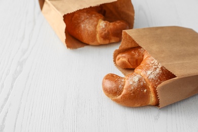 Paper bags with pastry on light wooden background. Space for text