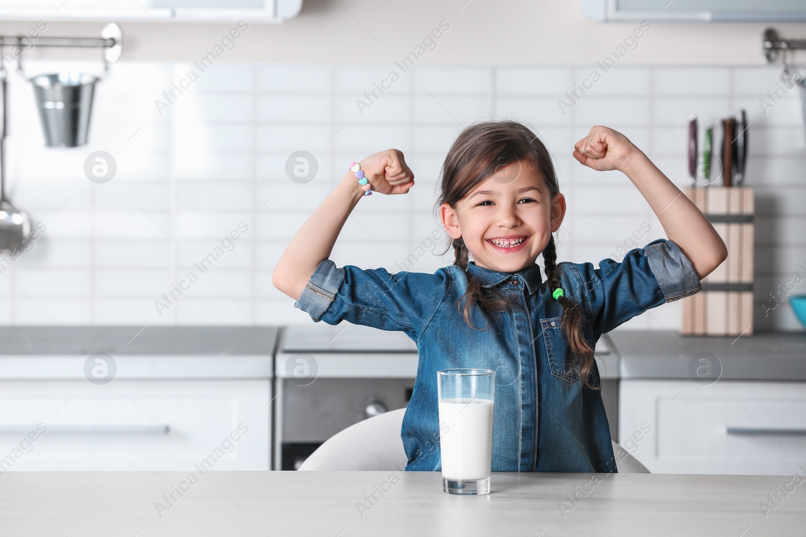 Photo of Cute little girl with glass of milk at table in kitchen