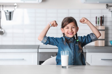 Cute little girl with glass of milk at table in kitchen