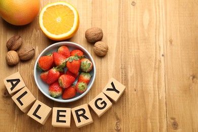 Image of Food allergy. Walnuts, strawberries, citrus fruits and cubes on wooden table, flat lay with space for text