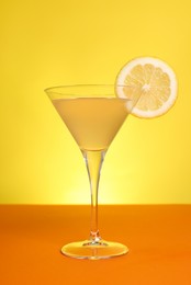 Photo of Martini glass of refreshing cocktail with lemon slice on orange table