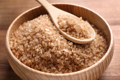 Photo of Bowl and spoon with brown sea salt on wooden table, closeup. Spa treatment