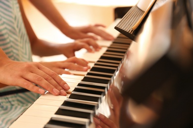 Young woman teaching little girl to play piano indoors, closeup