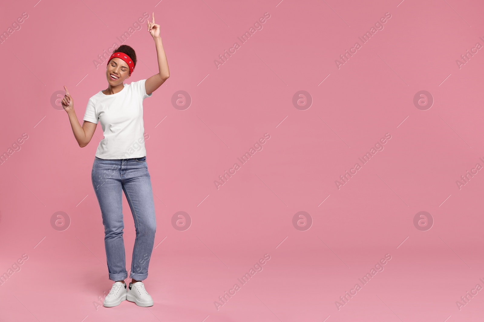 Photo of Happy young woman in stylish headband dancing on pink background. Space for text