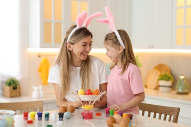 Photo of Easter celebration. Happy mother and her cute daughter with painted eggs at white marble table in kitchen