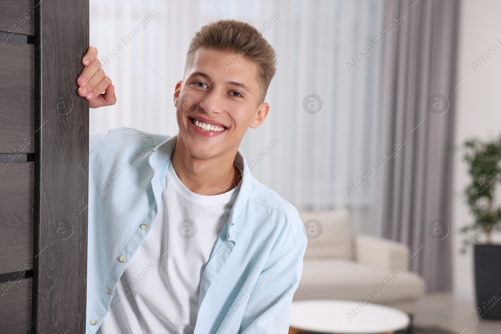 Photo of Happy man standing near door, space for text. Invitation to come indoors