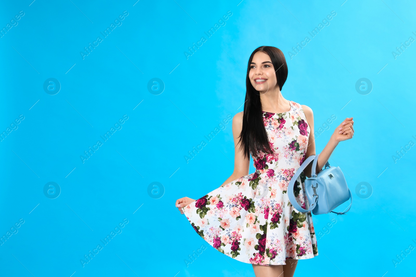 Photo of Young woman wearing floral print dress with stylish handbag on light blue background. Space for text