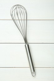 Metal whisk on white wooden table, top view