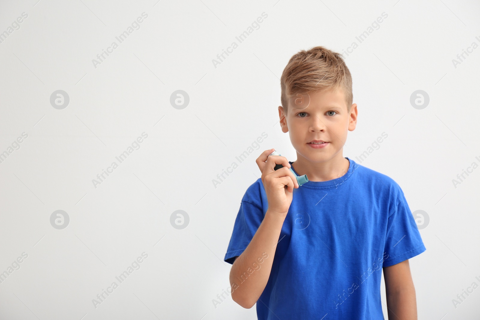 Photo of Little boy with asthma inhaler on light background