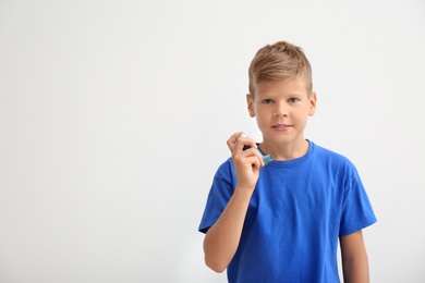 Photo of Little boy with asthma inhaler on light background