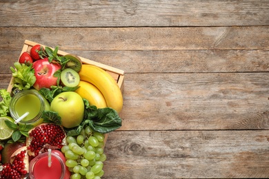 Photo of Wooden crate with juices in mason jars and fresh fruits on wooden background, top view. Space for text