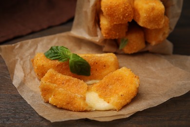 Photo of Tasty fried mozzarella sticks and basil leaves on wooden table, closeup
