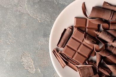 Photo of Plate with chocolate curls and pieces on grey background, top view. Space for text