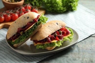 Photo of Delicious sandwiches with bresaola, cheese and lettuce on light blue wooden table