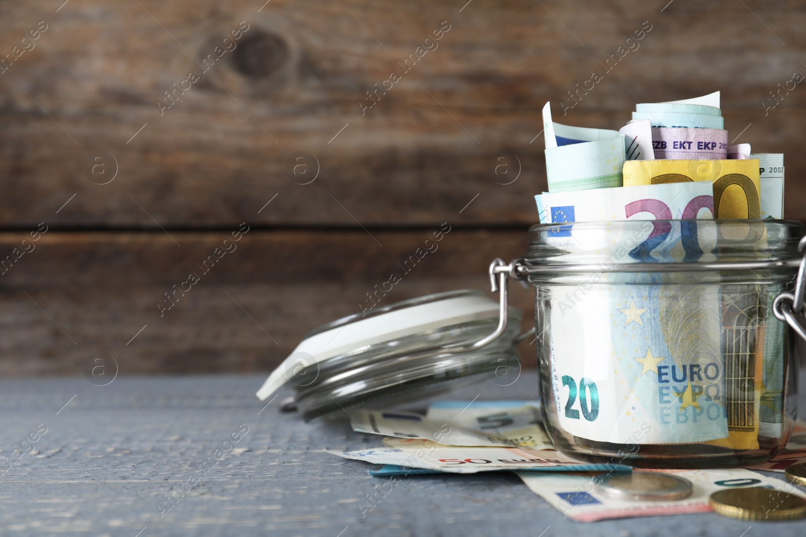 Image of Glass jar full of money on wooden table. Space for text 