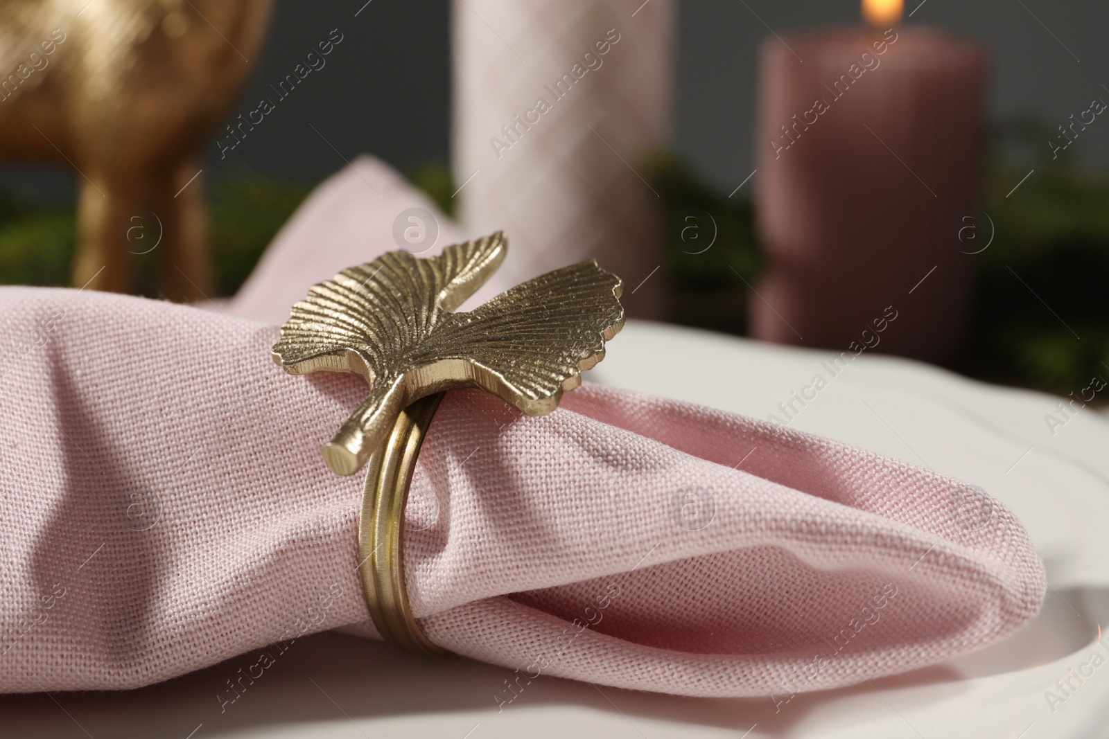 Photo of Pink fabric napkin with beautiful decorative ring for table setting on plate, closeup