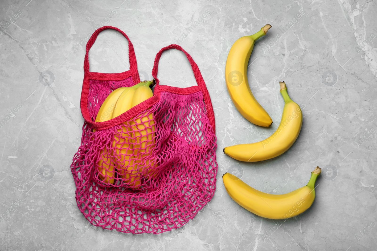 Photo of Net bag with fresh ripe bananas on light grey marble table, flat lay