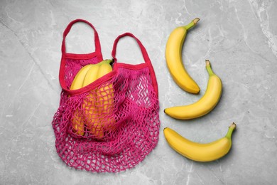 Photo of Net bag with fresh ripe bananas on light grey marble table, flat lay