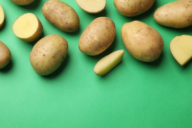 Photo of Fresh raw potatoes on green background, flat lay. Space for text