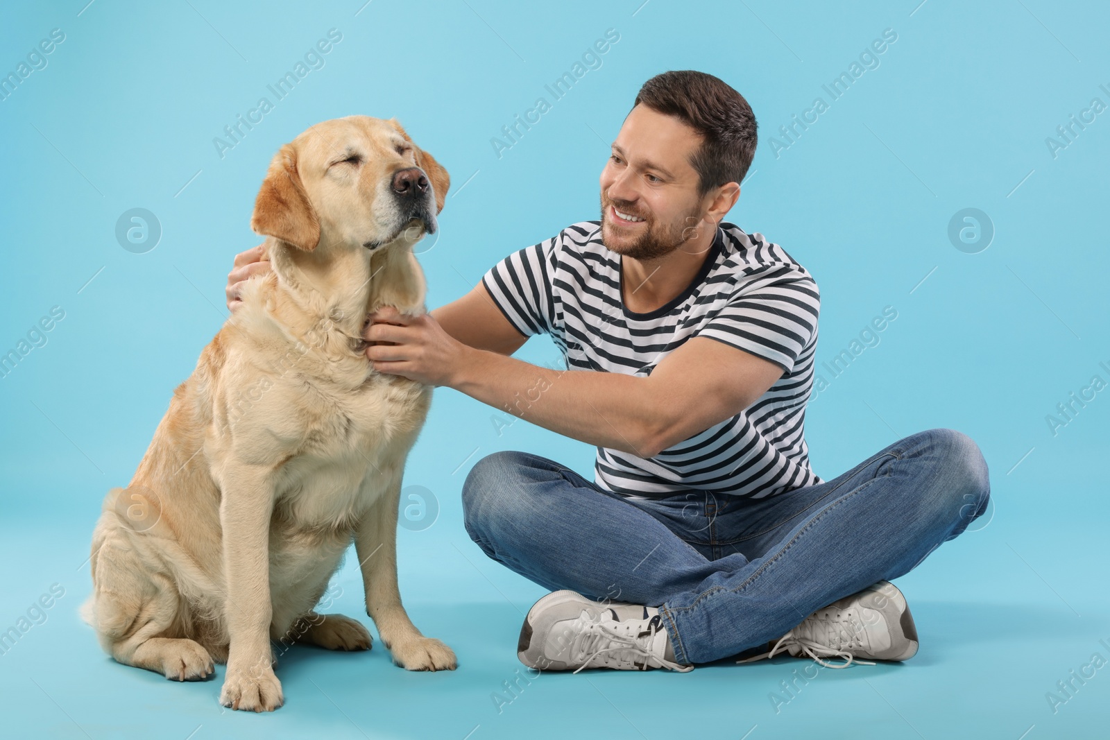 Photo of Man with adorable Labrador Retriever dog on light blue background. Lovely pet