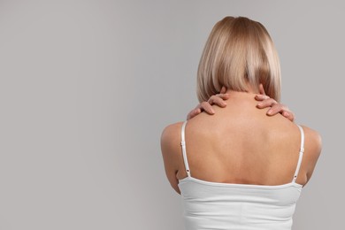 Photo of Woman suffering from pain in her neck on grey background, back view. Space for text