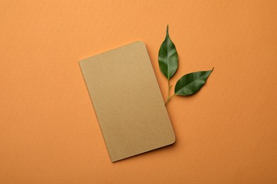 Kraft planner and green leaves on orange background, flat lay