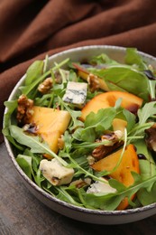 Photo of Tasty salad with persimmon, blue cheese and walnuts served on wooden table, closeup