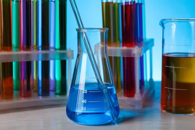 Photo of Different laboratory glassware with colorful liquids on wooden table against light blue background, closeup