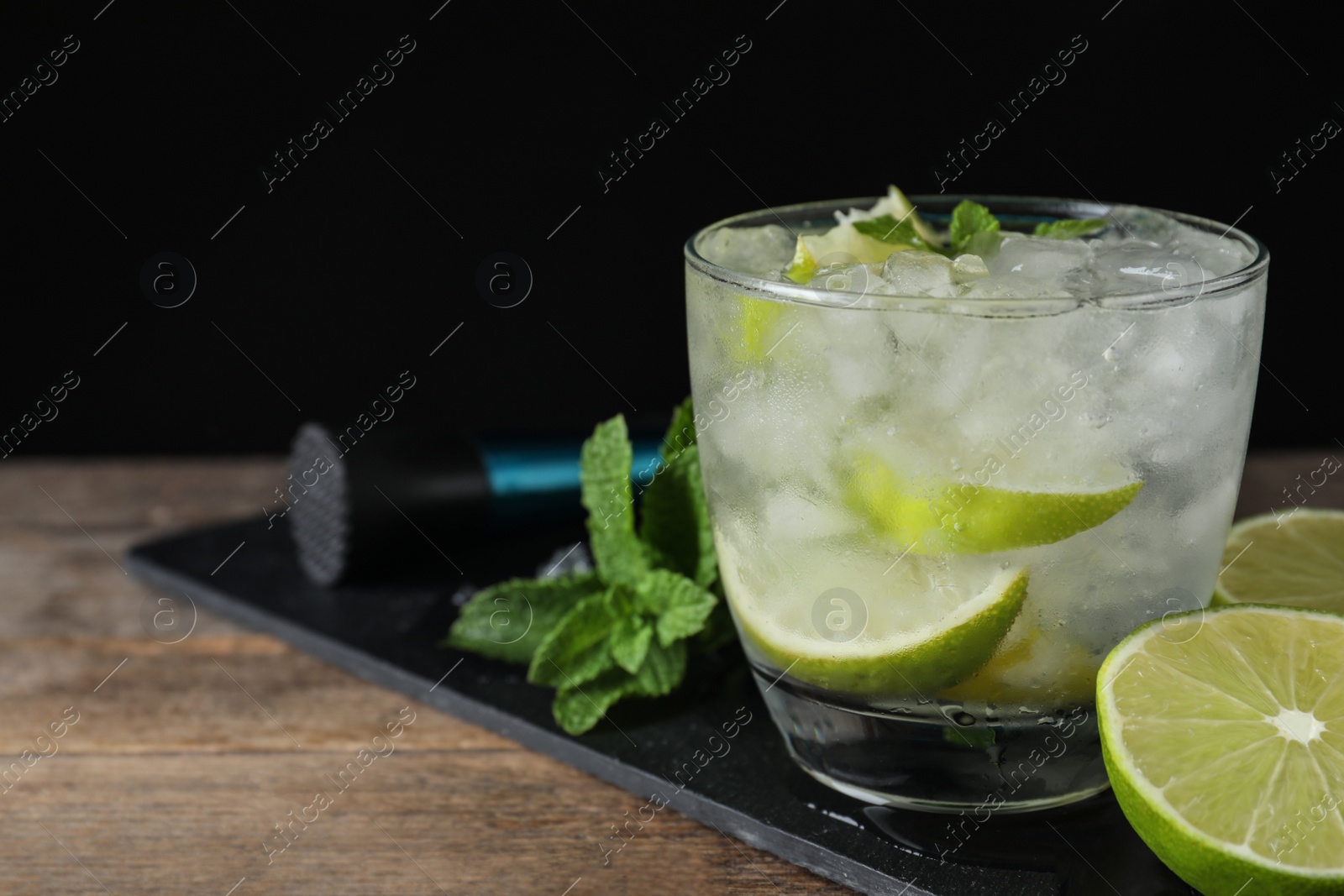 Photo of Glass of cocktail with vodka, ice and lime on wooden table against black background. Space for text