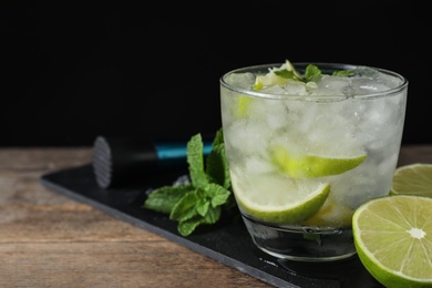 Glass of cocktail with vodka, ice and lime on wooden table against black background. Space for text