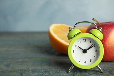 Alarm clock, orange and apple on light blue wooden table, space for text. Meal timing concept